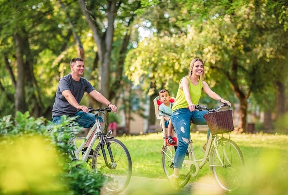 A white family ride bikes in a park