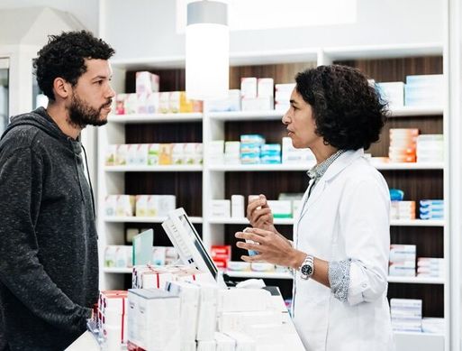 A female pharmacist talks to a male customer in a pharmacy.