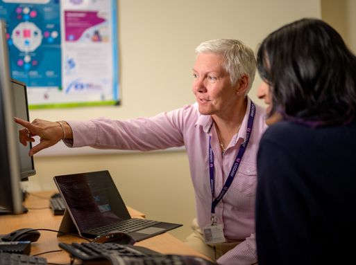 A white older woman with short white hair pointing to something on a computer screen in an office.
