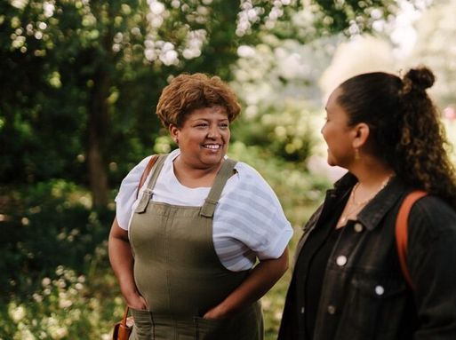 Two women are walking through a park smiling.