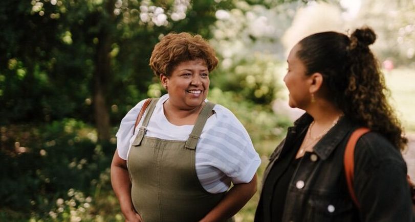 Two women are walking through a park smiling.