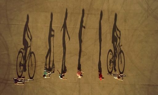 Shadows of people cycling, scooting and roller skating stretch out across a playing field.