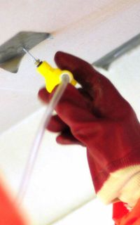 A person in a hazmat suit testing a ceiling for asbestos using tubes.