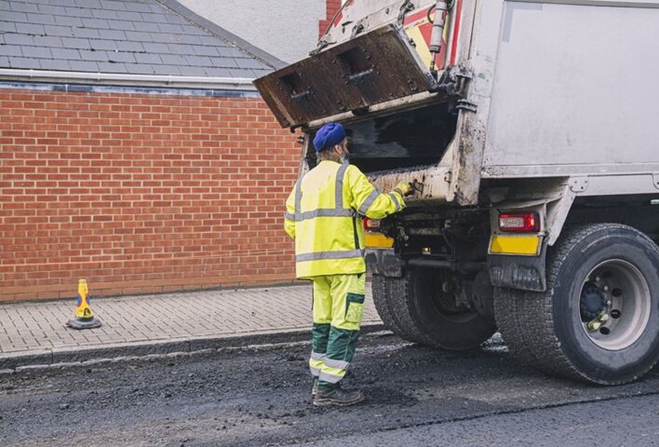 A refuse collector collects rubbish and puts it into a van. He is wearing high vis clothing.
