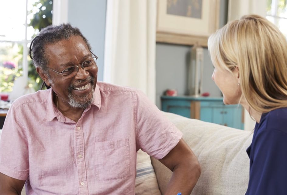 Smiling man talking with a woman during a relaxed conversation in a cozy, well-lit living room.