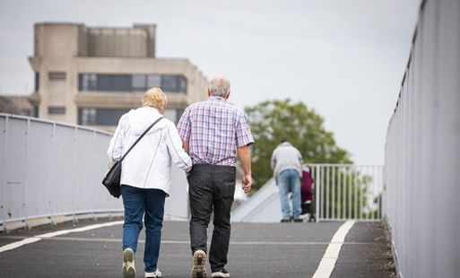 An elderly couple walk across a pedestrian bridge.