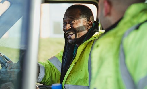 Man behind the wheel of van smiling in a high-vis jacket.