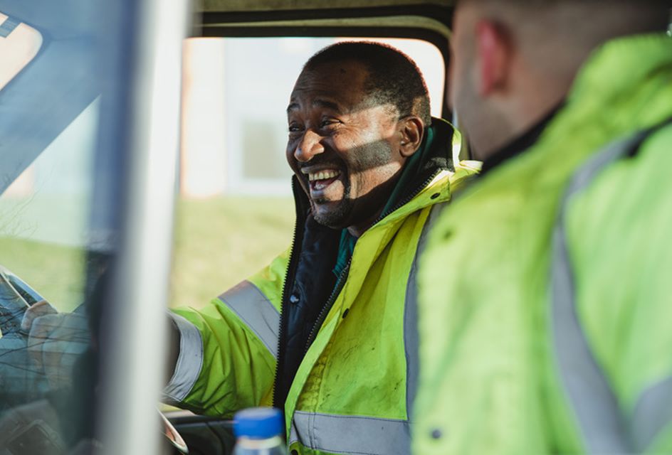 Man behind the wheel of van smiling in a high-vis jacket.