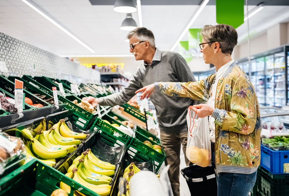 An older white couple picking out fruit and vegetables at a supermarket.