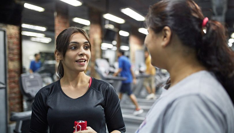 A health coach talks to another woman in a gym.