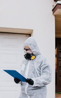 A person in a hazmat suit and respirator looking at a clipboard