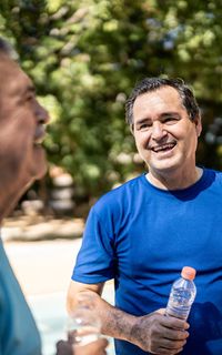 Two men chat in a park. One of them holds a water bottle.