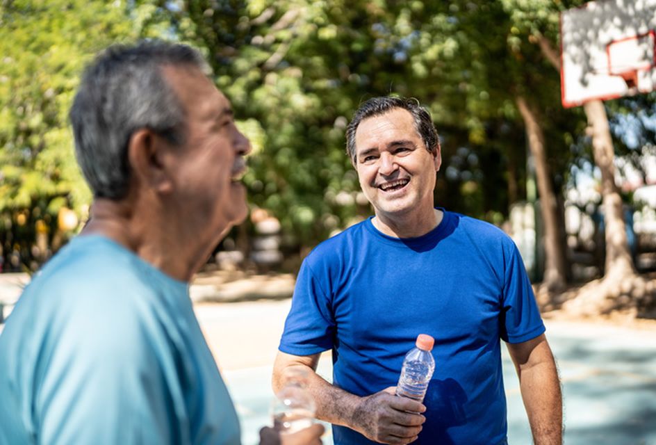 Two men chat in a park. One of them holds a water bottle.