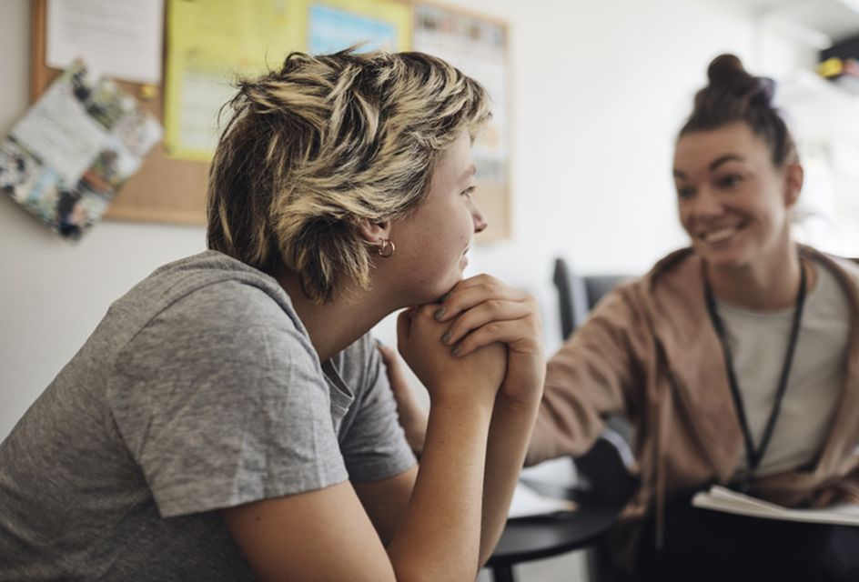 A counsellor wearing a lanyard talks to a young woman.