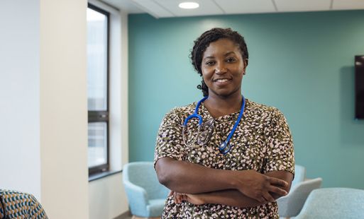 Female doctor wearing stethoscope with crossed arms smiling at the camera in a clinical waiting room.