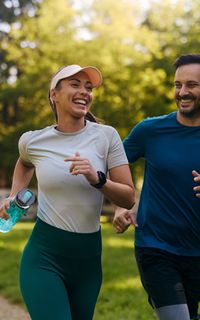 A white man and woman wearing sports clothes going for a run together in a park.
