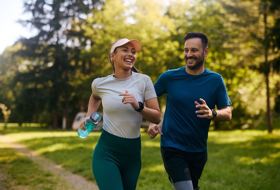 A white man and woman wearing sports clothes going for a run together in a park.