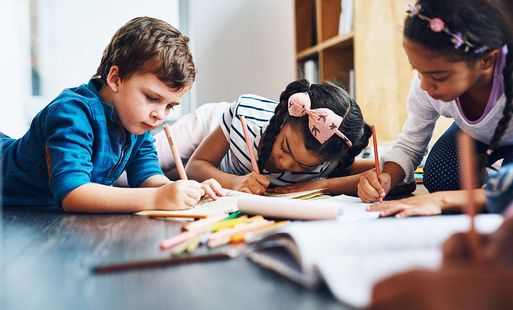 A group of children writing and drawing in notebooks with coloured pencils.
