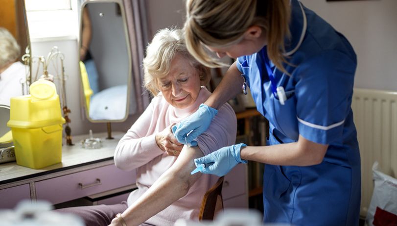 A nurse gives a plaster to an elderly woman after administering a vaccine.