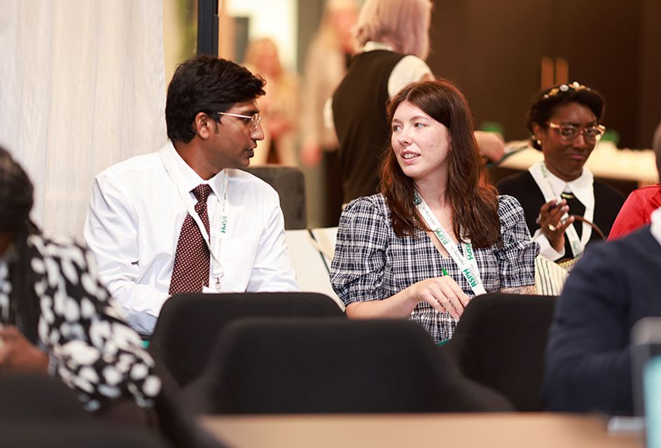 A man and a woman talking at a conference. They both wear RSPH lanyards.