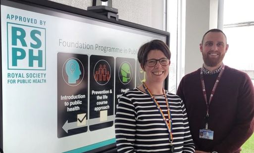 Two people stand beside a screen displaying "Foundation Programme in Public Health" and the Royal Society for Public Health approval logo.