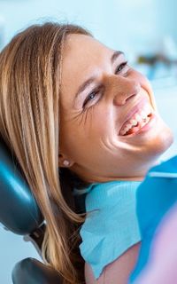 A woman smiles while sitting in a dentist chair