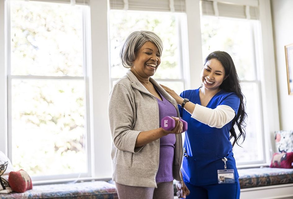 Smiling older woman doing physical therapy exercises with female physiotherapist at home