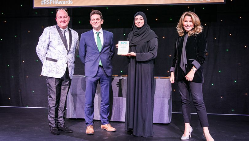 Four people stood on stage with two middle accepting an Award from Natasha Kaplinsky