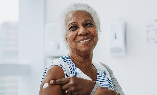 Older women smiling pointing at plaster on arm having just been vaccinated.