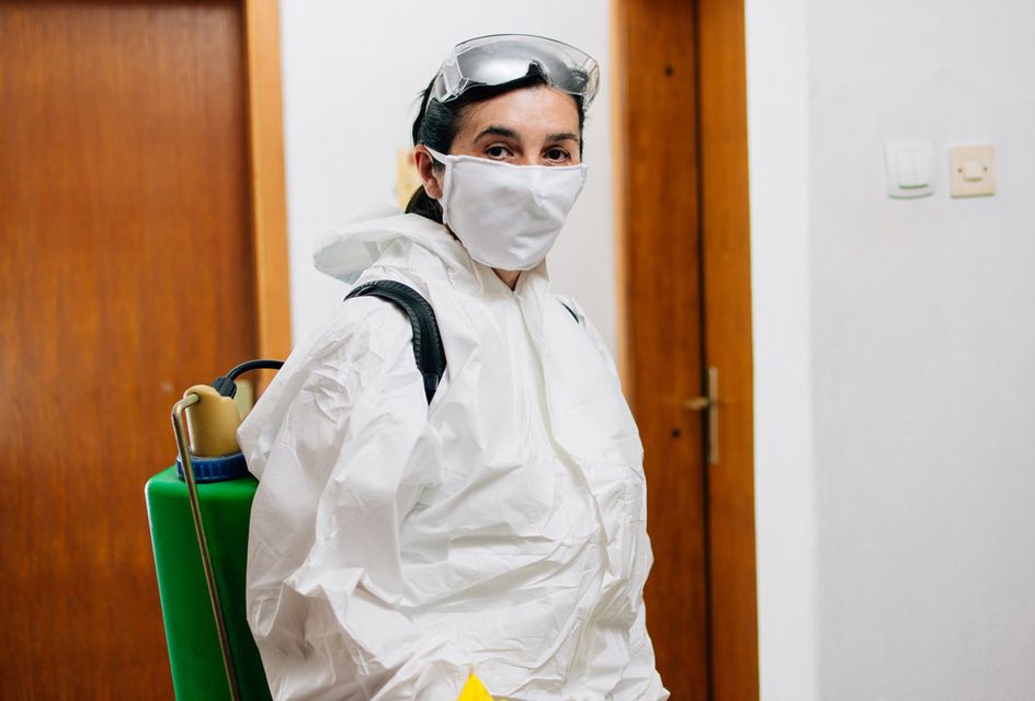 A female pest controller wearing protective clothing and a face mask