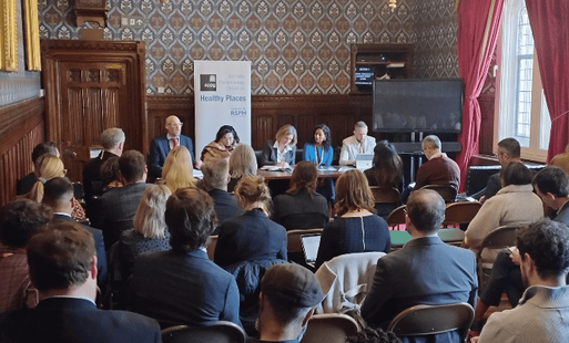 Panel discussion in a room in the houses of parliament with patterned wallpaper and red curtains.